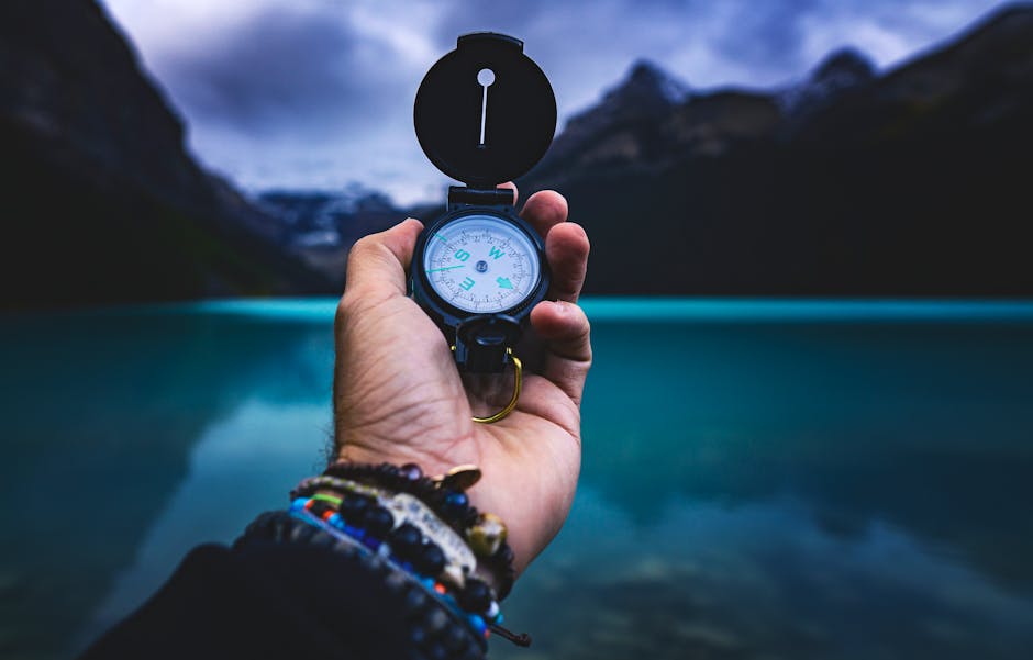 A hand holding a compass with a serene lake and mountains in the background, capturing the spirit of adventure.